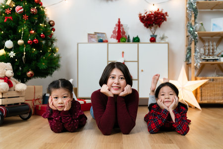 portrait of lovely asian family lying prone on floor and propping their faces while looking camera with smiles in festive living room with Christmas decorationsの写真素材