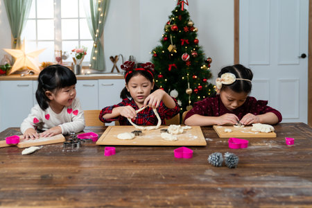 front view of an innocent asian baby girl looking at her older sister shaping dough as they are making ginger cookies together for Christmas in the kitchen at homeの写真素材