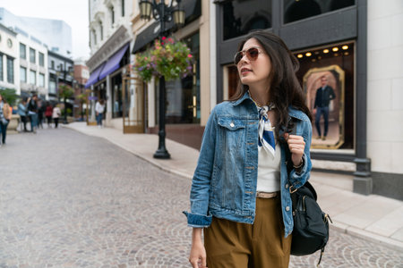 Asian woman with black hair wearing sunglasses walking on city streets while doing shopping outdoors. Sales and discounts concept.の写真素材
