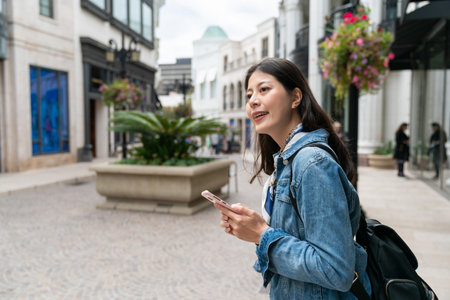 asian girl exchange student consulting guide on phone and looking into space for the shop wants to visit during her stay in Beverly hillsの写真素材