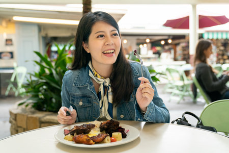 Smiling beautiful young happy Korean woman eating steak meal outdoors on beautiful day. Concept of cuisine and lifestyle.の写真素材