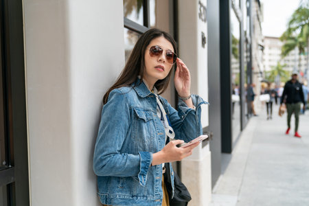asian japanese lady in sunglasses is looking far with her phone in hands.の写真素材