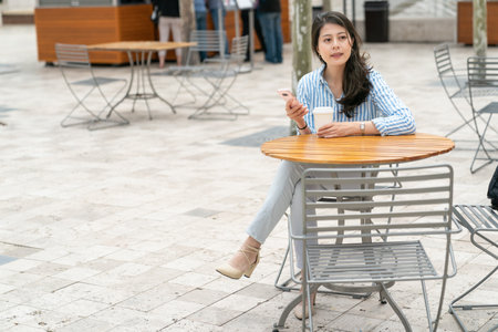 attractive asian Japanese woman manager looking at streetscape while relaxing at outdoor dining area in the city of los angeles united statesの写真素材