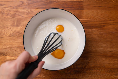 Organic homemade eggs in a bowl with kefir or milk. Cooking. Whisk in female handsの写真素材