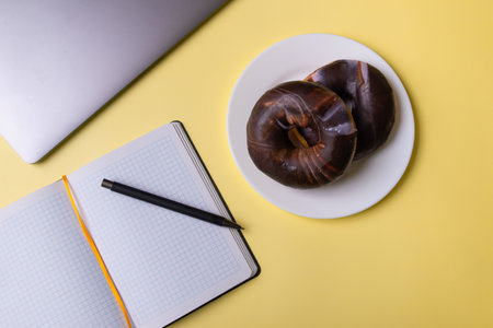 Laptop, notebook and donut on a white plate, top view. Place for text