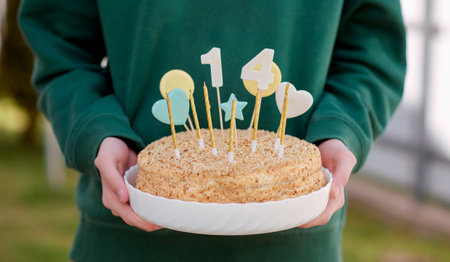 A man stands holding a cake with candles in it. 14 years old, a teenager. Birthday cake.