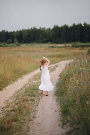 The girl runs along the forest road. Summer evening field and childの写真素材
