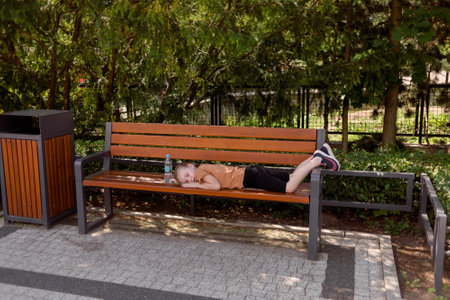The child is tired of walking and lies on a bench resting, there is a bottle of drinking water nearbyの写真素材