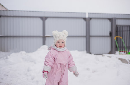 A girl playing in winter on the street. A child in a winter jumpsuit playing snowballs.の写真素材