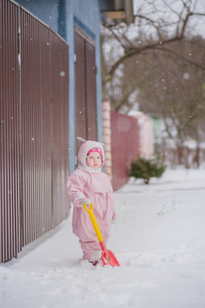 A girl playing in winter on the street. A child in a winter jumpsuit playing snowballs.の写真素材