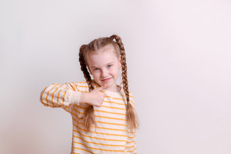 The cheerful girl on the white wall makes a thumbs up gestureの写真素材