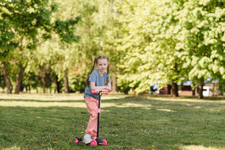 portrait of a little girl riding a scooter in a pakr in natureの写真素材