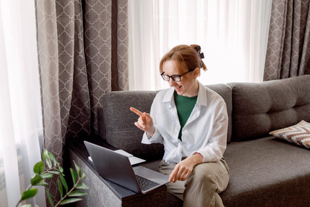 Pretty womanusing laptop elearning or remote working at home office looking at laptop computer watching webinarの写真素材