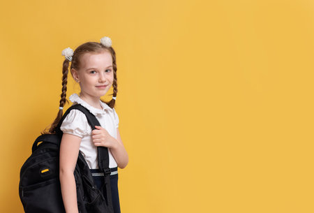 Girl schoolgirl is going after the holidays at school, standing on a yellow background with a...