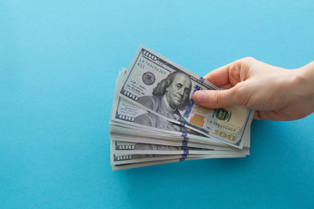 Hands holding dollars on a blue background with space for text
