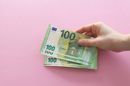 Hands holding euro on a pink background with space for text