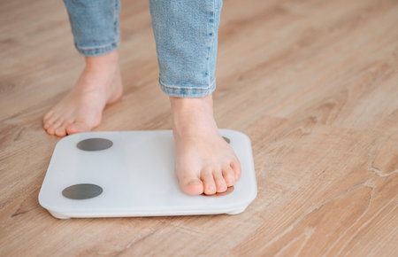 Young woman standing on scales at home. Weight loss concept. High quality photoの写真素材
