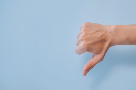 Hand showing thumbs down gesture on blue background with copy space, disapproval or dislike. High
