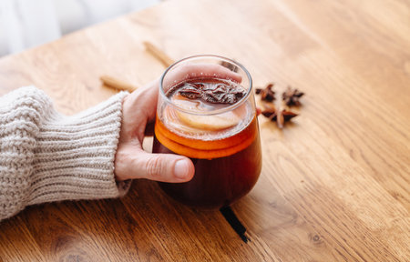 Woman in cozy sweater drinking hot mulled wine with oranges and cinnamon.の写真素材