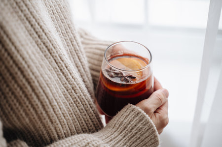 Woman in cozy sweater drinking hot mulled wine with oranges and cinnamon.の写真素材