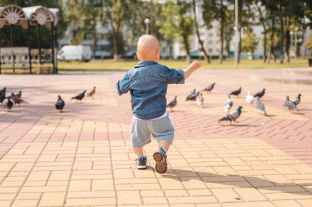 Little boy running after pigeons on city square, childhood fun moment.の写真素材
