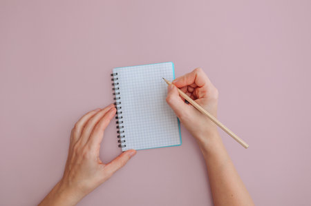 Girl writing with pencil on pink background, notebook mockup concept.