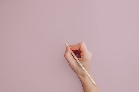 Hand holding a pencil on a pink background.の写真素材