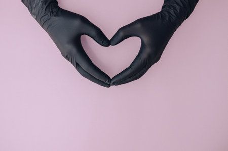 Hands in gloves forming heart shape on pink background, medical care symbol.の写真素材