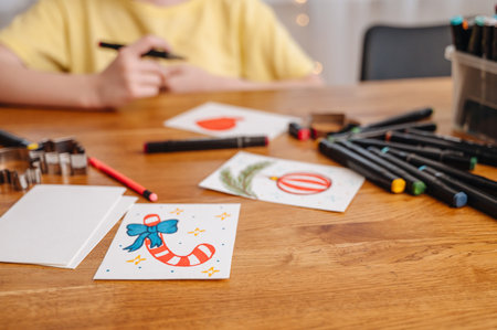 A young girl creatively making New Year greeting cards at home, using colorful markers on a table.