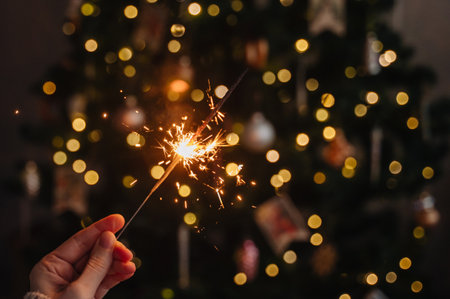 Hand holding a sparkler against blurred festive holiday lights backgroundの写真素材