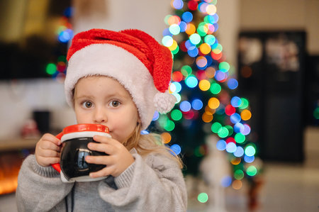 A cute girl with a mug at the table, a Christmas tree and a fireplace create a cozy festive...
