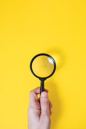 Hand holding a classic magnifying glass against a bright yellow background, discovery and search concept. High quality photo