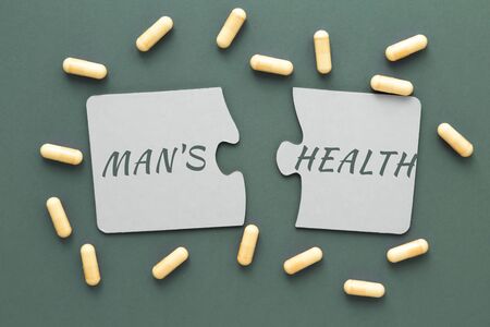 inscription man s health on white disconnected puzzles, yellow pills on a green backgroundの写真素材