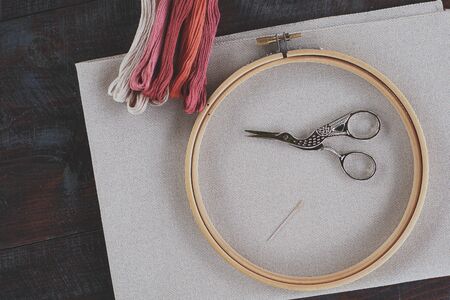 Canvas for embroidery with a cross embroidered in a round wooden hoop, multi-colored thread mouline thread, needle, scissors for needleworkの写真素材