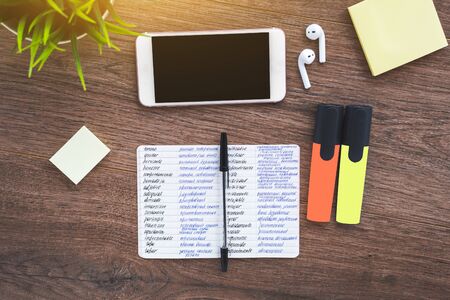 Notebook for writing foreign words dictionary, smartphone, wireless headphones on a wooden brown desktopの写真素材