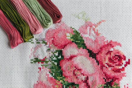 The process of cross-stitch on a white canvas Hades and thread floss