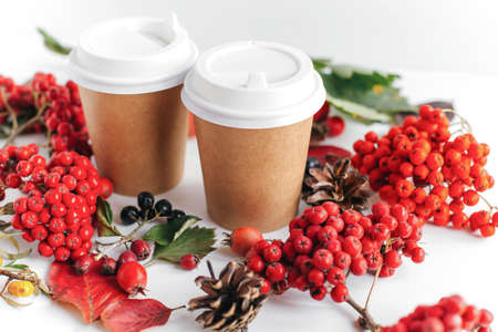 two paper glasses for hot drinks among autumn leaves, berries and cones, autumn concept