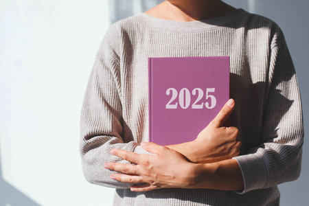 young woman in beige sweater holds lilac diary with 2025 inscription in her hands, her face is not visible, concept of planning and goals for new year.の写真素材