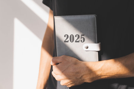 male hand holding a diary with the inscription 2025 on the background of a black T-shirt, concept of planning goals and plans for the new year.の写真素材