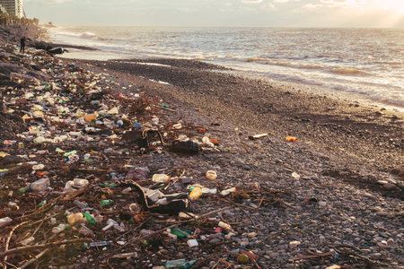 Polluted beach covered with waste, bottles, and debris washed plastic ashore. Ocean waves in the...