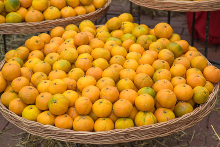 Close-up of ripe oranges piled in woven baskets at outdoor market. The vibrant orange tangerines hues contrast with hints of green, creating a fresh and natural composition. Rustic organic atmosphereの写真素材