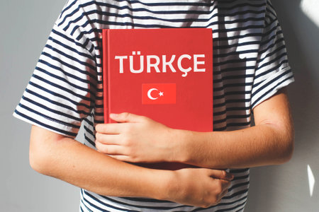 One child girl, whose face is not visible holds a red Turkish language textbook with text Turkish in Turkish and Turkey flag, foreign language learning concept.の写真素材