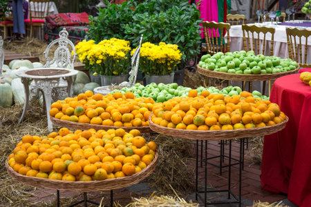 Fresh oranges and green apples are neatly arranged in wicker baskets at an outdoor market. Vibrant yellow flowers and rustic decor create a cozy atmosphereの写真素材