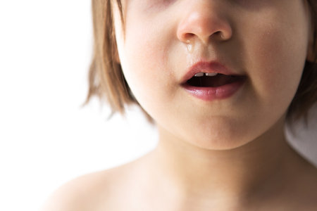 Close-up of young child's 2-3 years mouth and nose with visible runny nose and slightly open lips, showing signs of illness or emotional distress against bright backgroundの写真素材