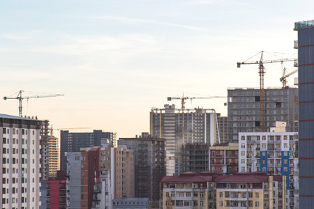 Urban cityscape with multiple tower cranes and high-rise buildings under construction at sunset, concept of architecture, development, urbanizationの写真素材
