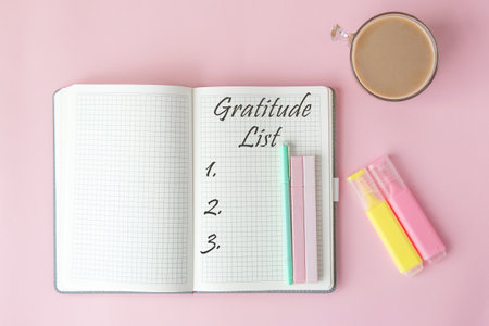 Open notebook with handwritten gratitude list, pastel pens and markers on pink background, flat lay composition with cup of coffee, concept of mindfulness and self-care conceptの写真素材