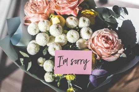 Bouquet of pastel flowers wrapped in blue paper with a pink apology card that says I'm sorry. Soft sunlight highlights the delicate petals. Concept of apology, forgiveness, and heartfelt emotionsの写真素材