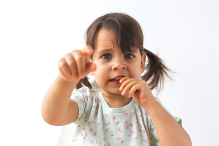 A little girl with pigtails eating a carrot while pointing forward with a determined expression. Her...