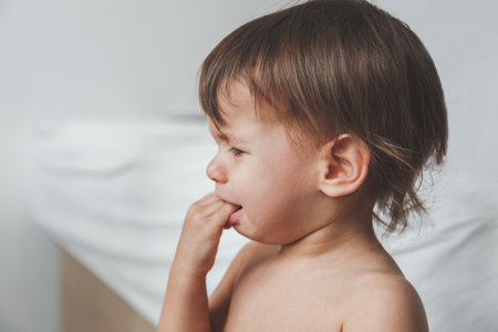 photo of a little baby girl in profile who is crying and puts her hands in her mouth on a white background, the child is teething.の写真素材