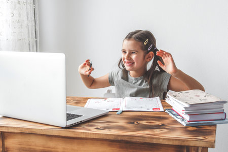 cheerful laughing girl 7 years old studying online at school, video call with teacher, looking at...